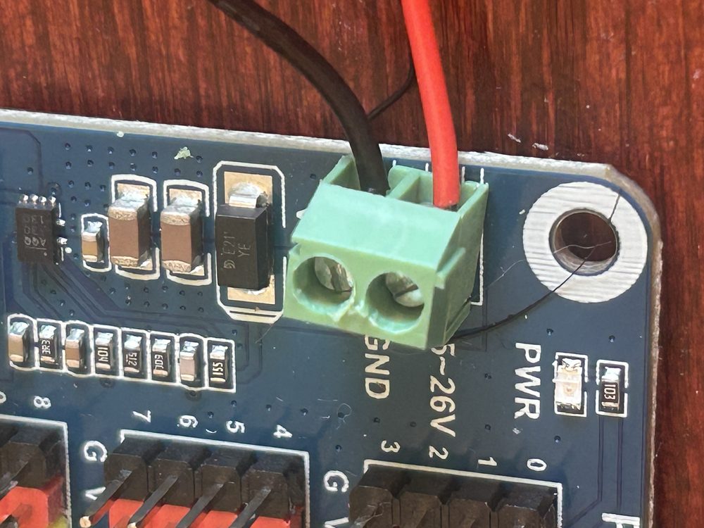 Close-up of the battery pack's red and black wires seated in the board's green screw terminal, red on the 4.5-26V pin, black on GND.