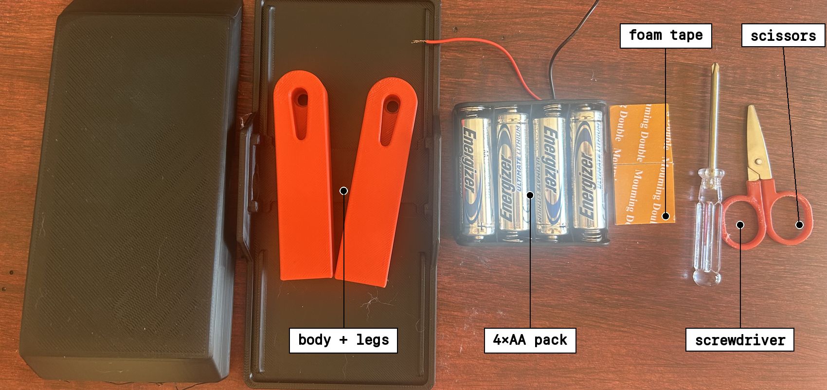 The 3D-printed body case and legs, a 4x AA battery pack with wire leads, orange foam mounting tape, a small Phillips screwdriver, and scissors standing in for a flat-head screwdriver.
